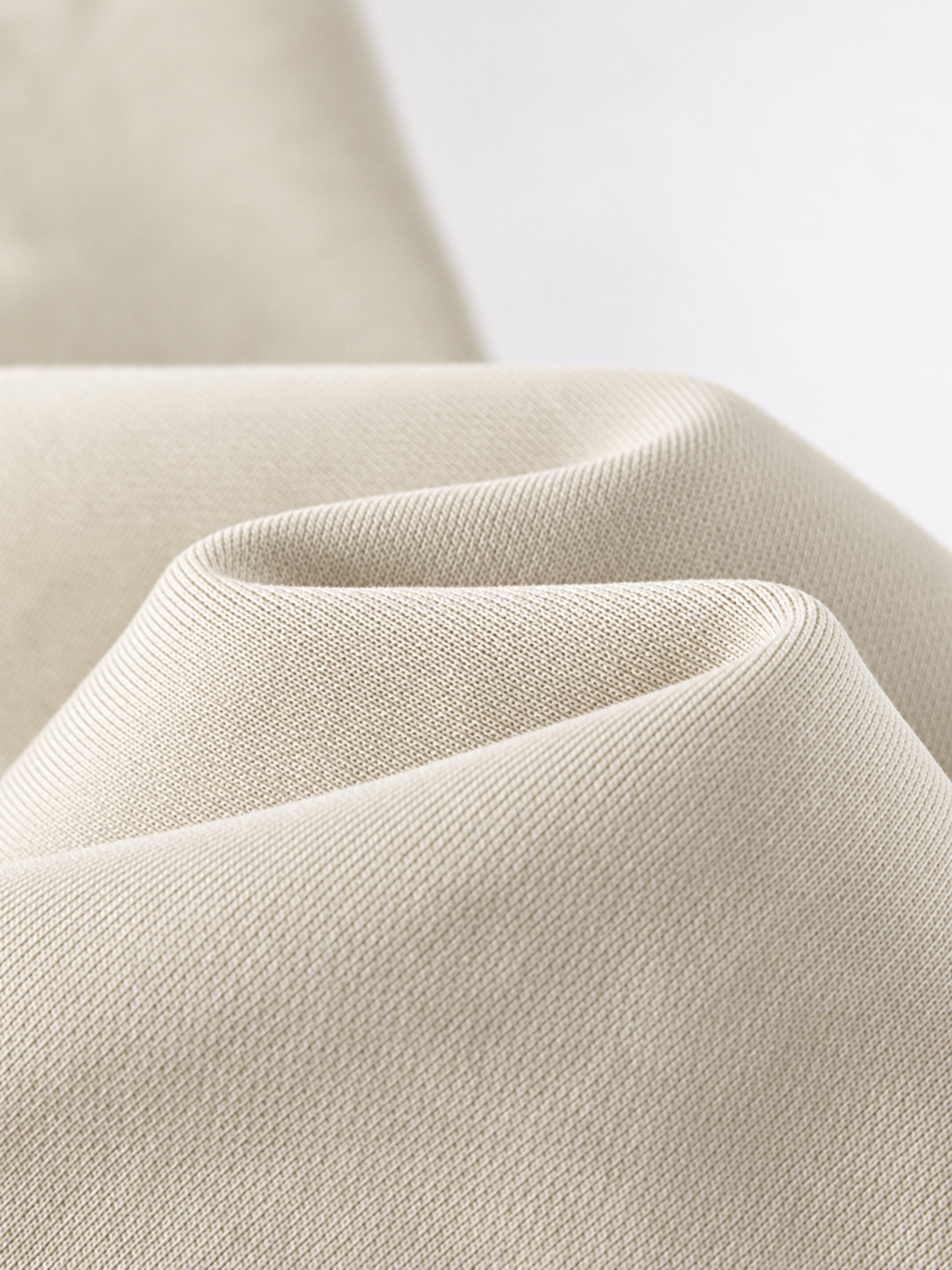 A close-up of draped light beige fabric with a fine woven texture, showing soft folds against a clean white background.
