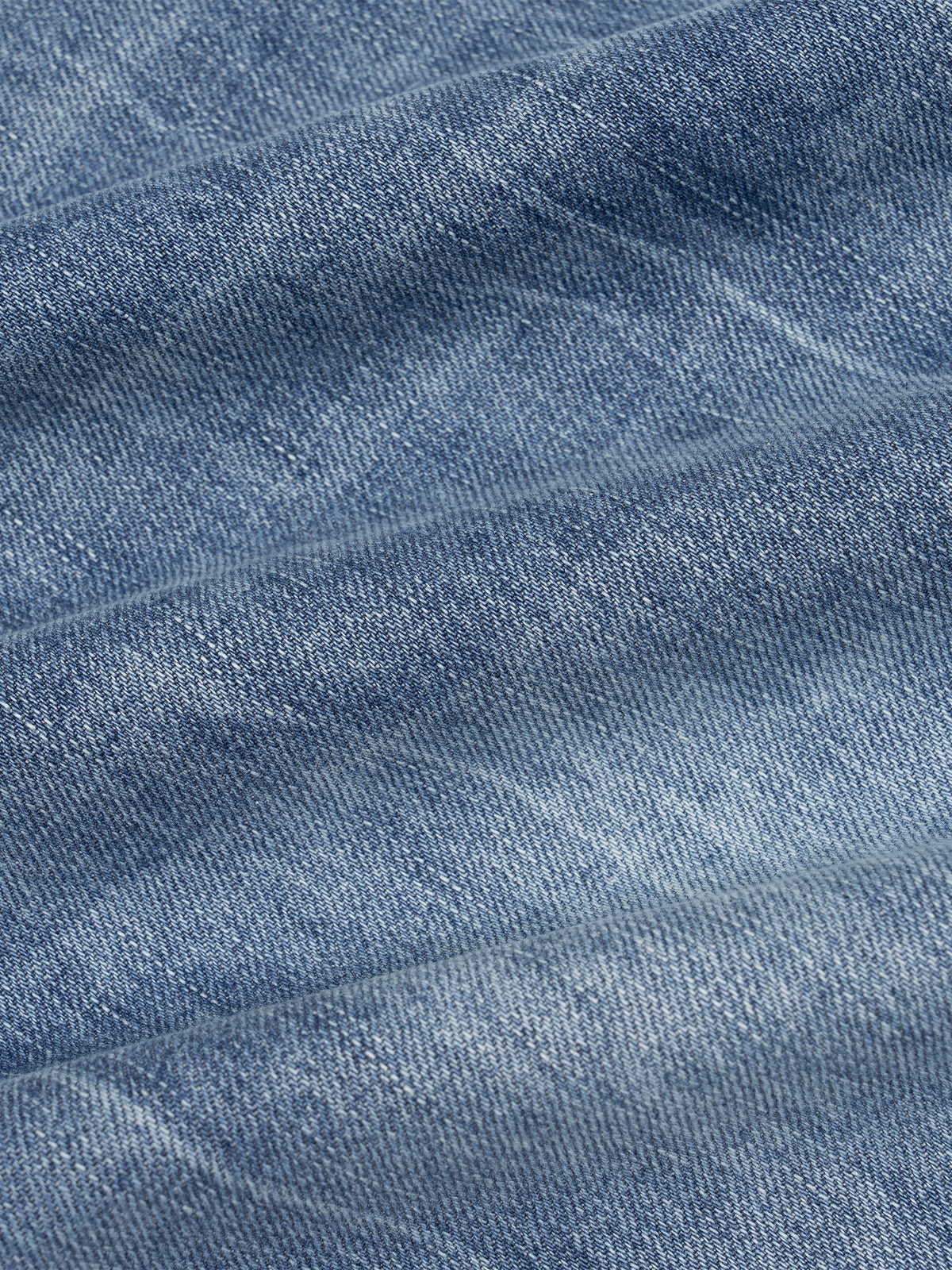 A close-up of textured blue denim fabric with soft folds and a slightly mottled wash.