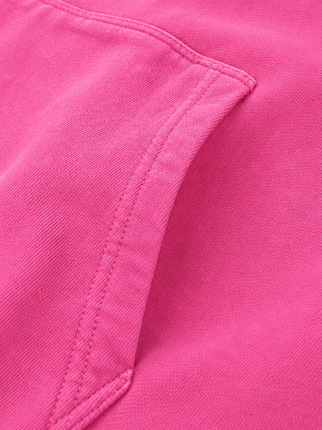A close-up detail shot of a bright pink garment, showing the texture of the fabric and a diagonal seam.