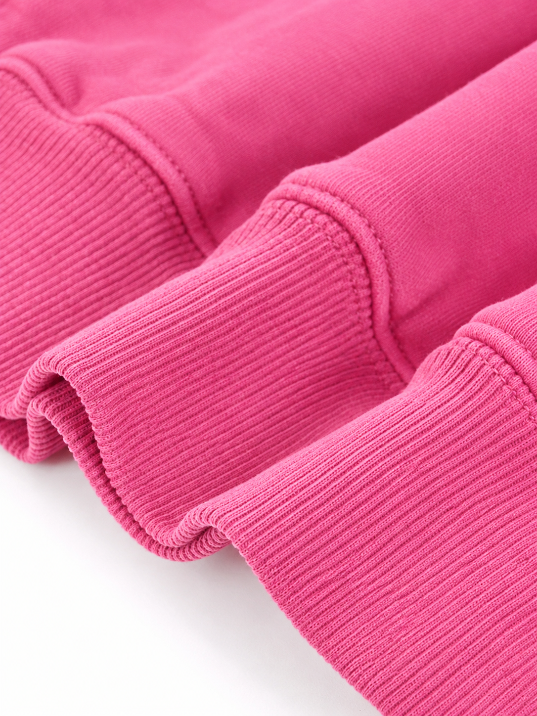 A close-up of bright pink ribbed fabric, showing the texture and folds of a garment or textile on a white background.