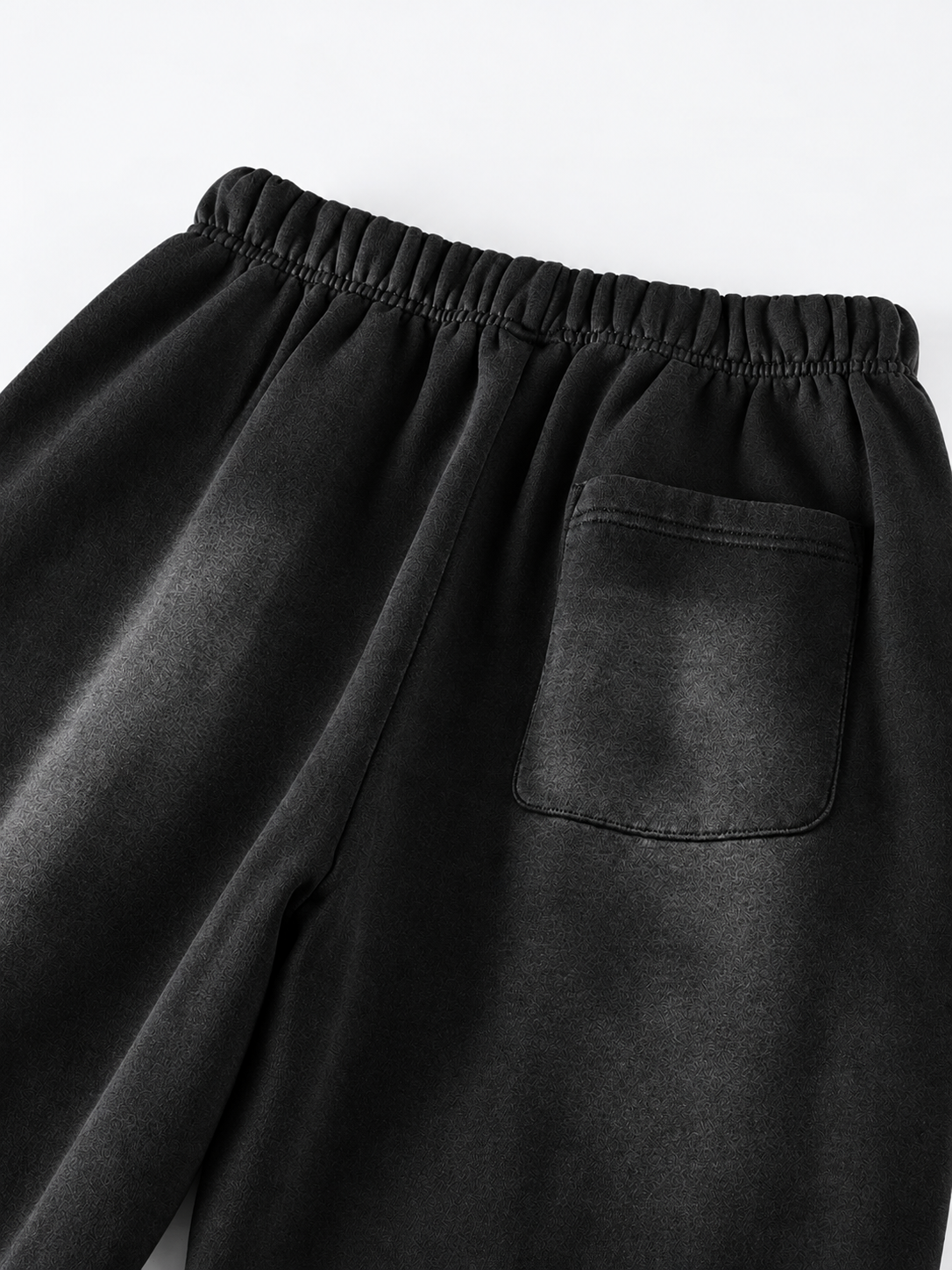 Close-up of black lounge pants showing an elastic waistband and a side pocket, photographed against a light gray background.