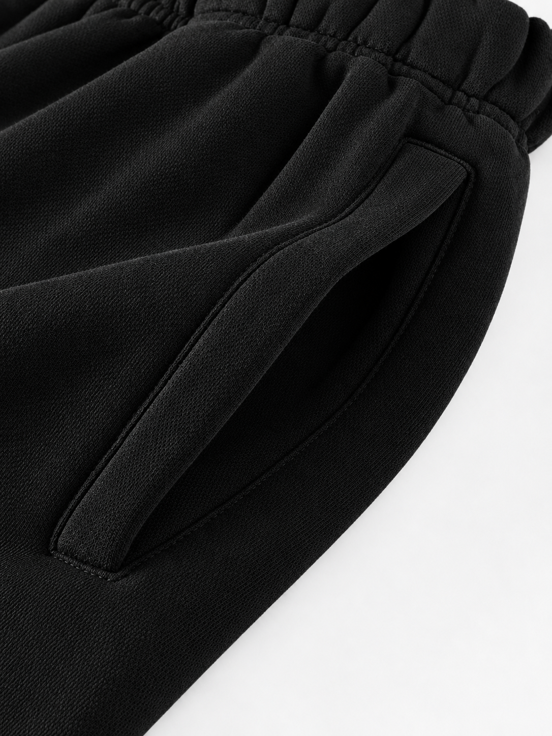 Close-up of black fabric with an elastic waistband and a side pocket, photographed on a white background.