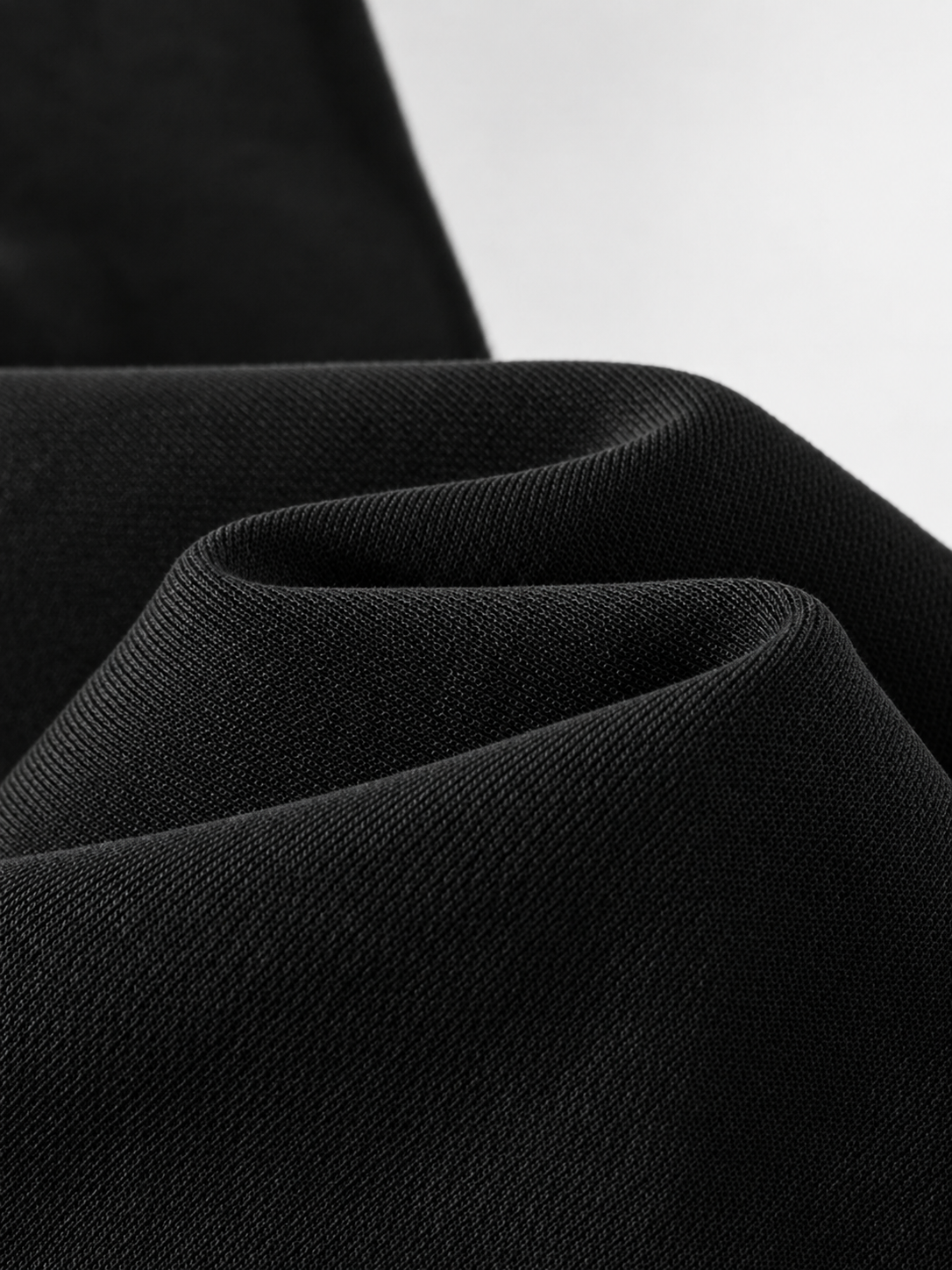 Close-up of draped black fabric with visible woven texture against a light gray background.