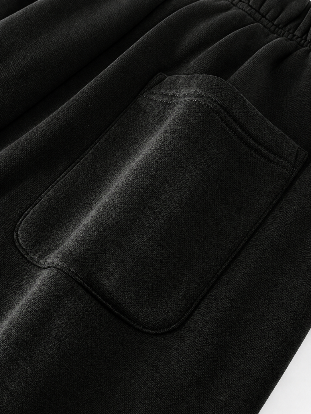 Close-up detail of black fabric clothing showing an elastic waistband and a large front patch pocket.