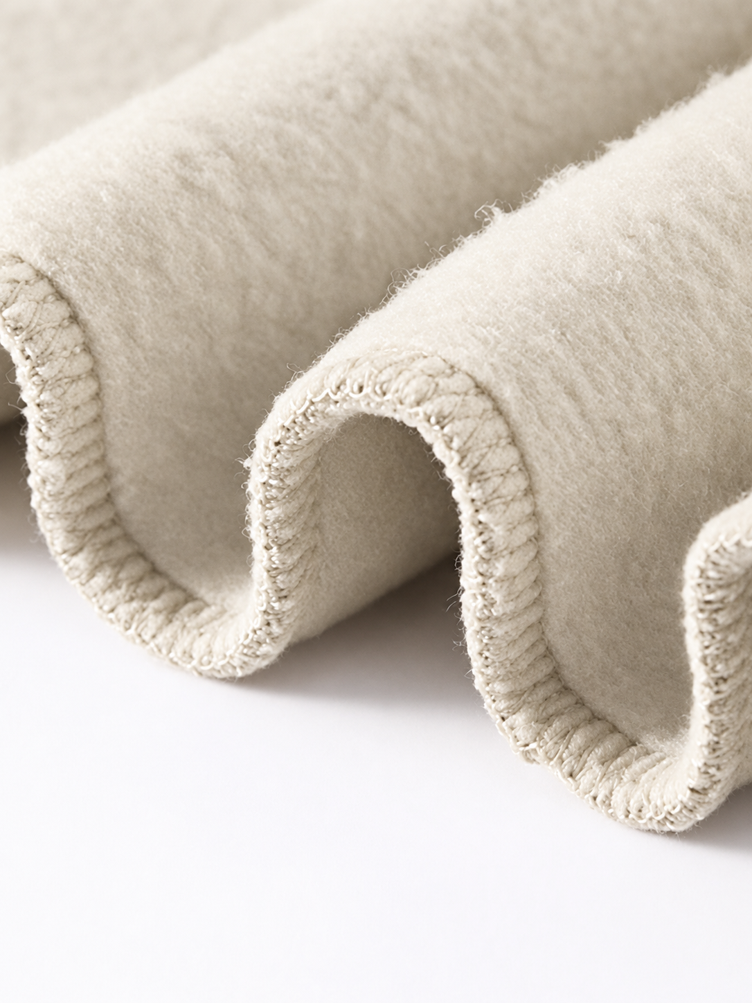 A close-up of a soft, rolled fabric or textile in a warm off-white/cream color, showing its fuzzy texture and ribbed edge on a plain white background.