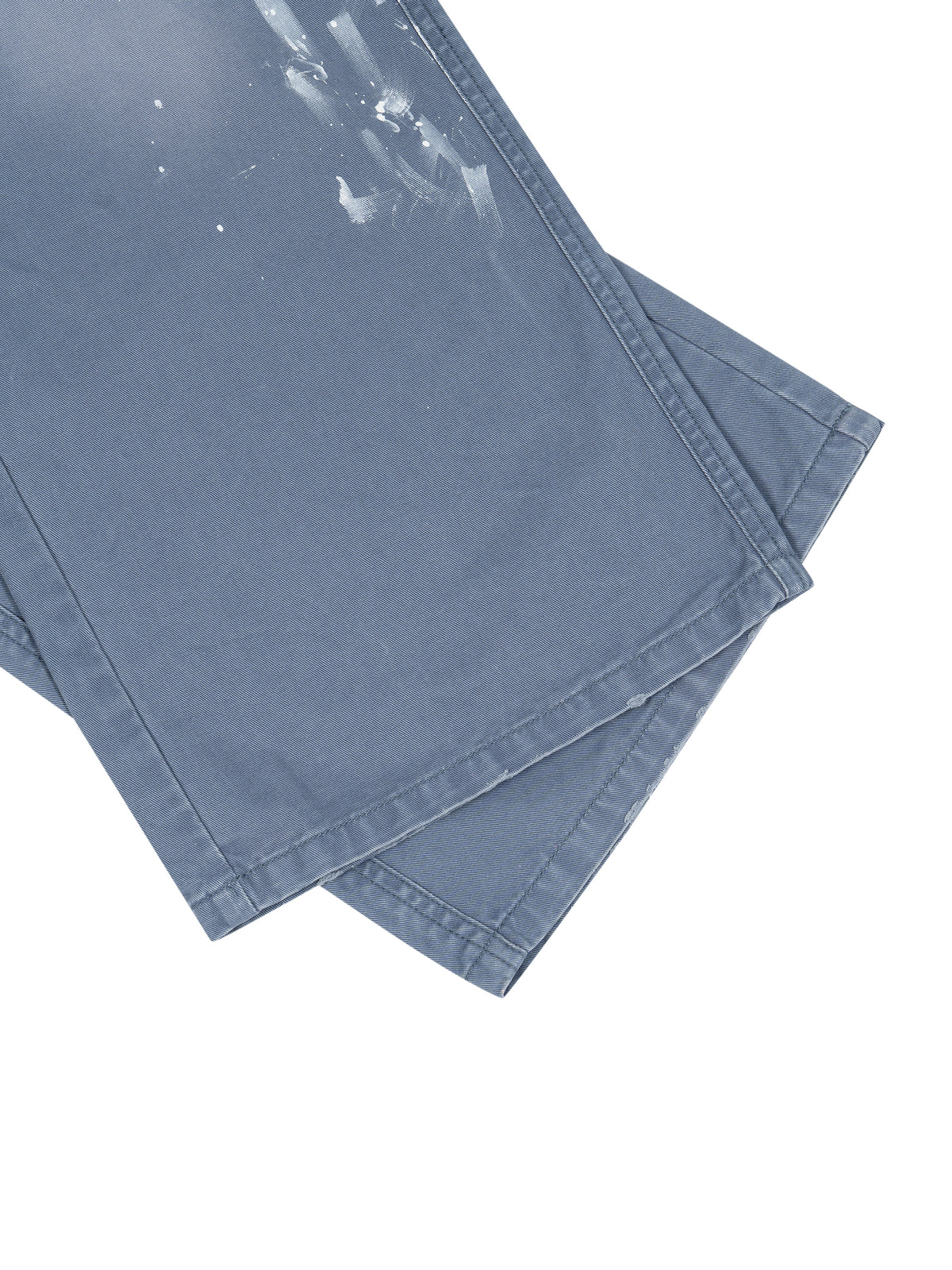A close-up of folded blue denim jeans with white paint splatters on the fabric, set against a plain white background.