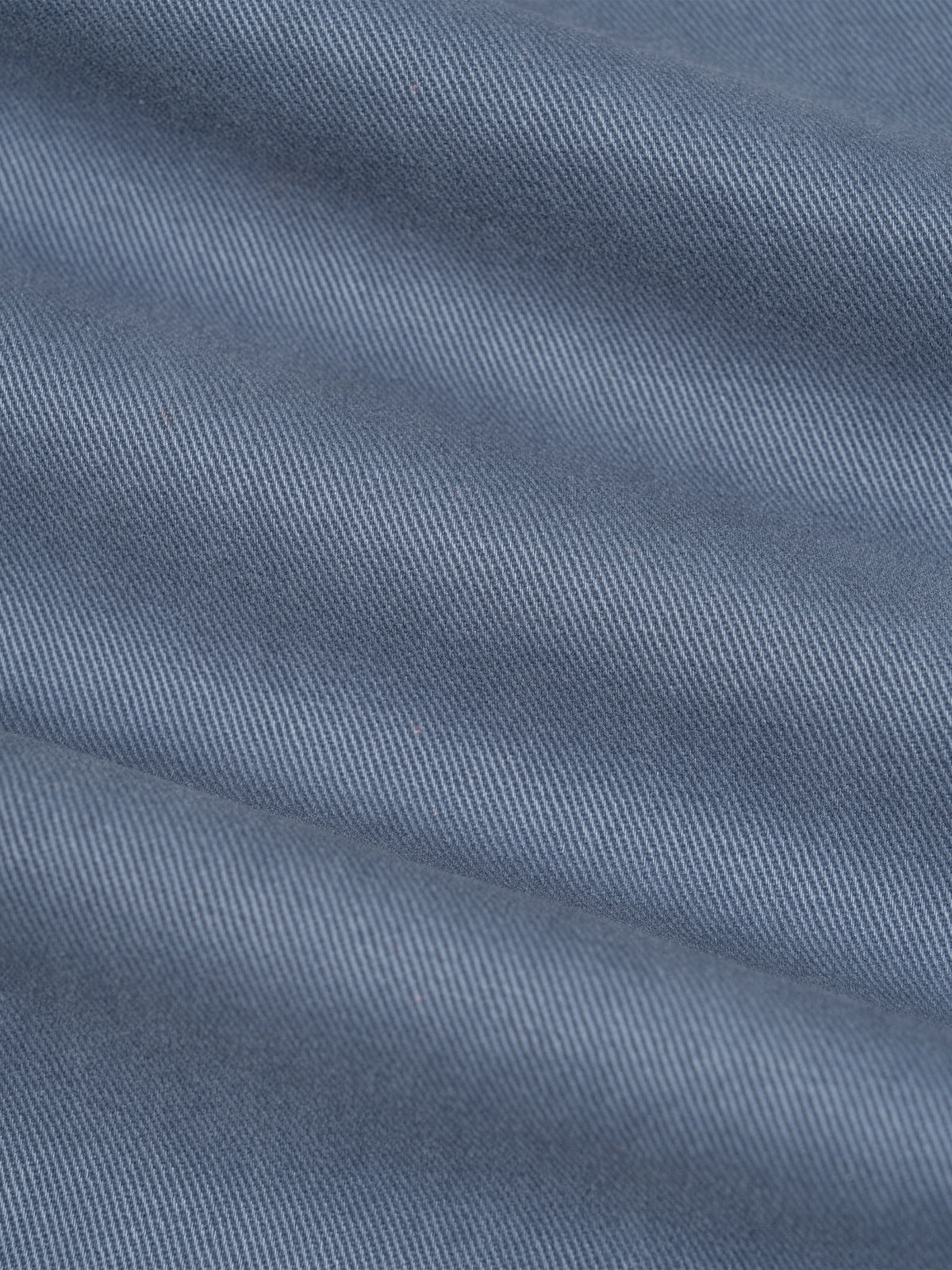 A close-up of textured fabric in a muted dusty blue color, showing the weave and soft folds.