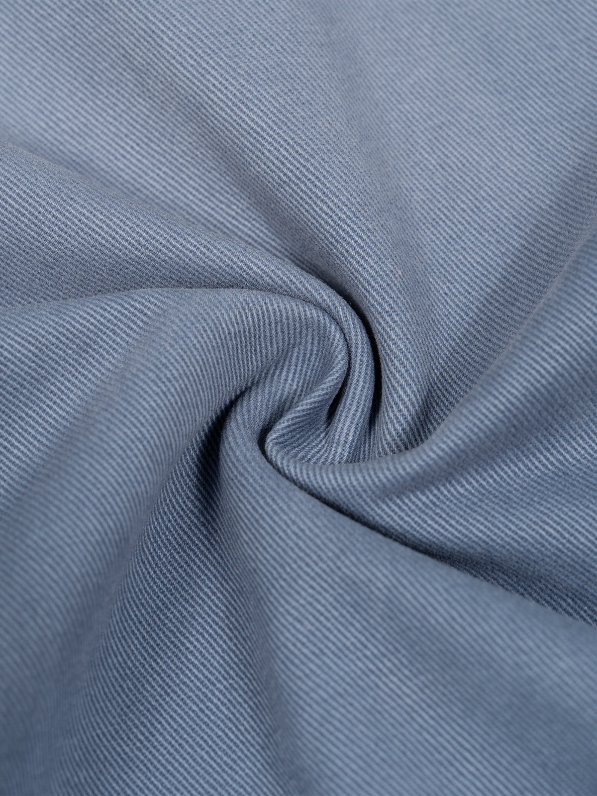 A close-up of textured blue-gray fabric with a subtle diagonal twill weave, artistically swirled in the center.