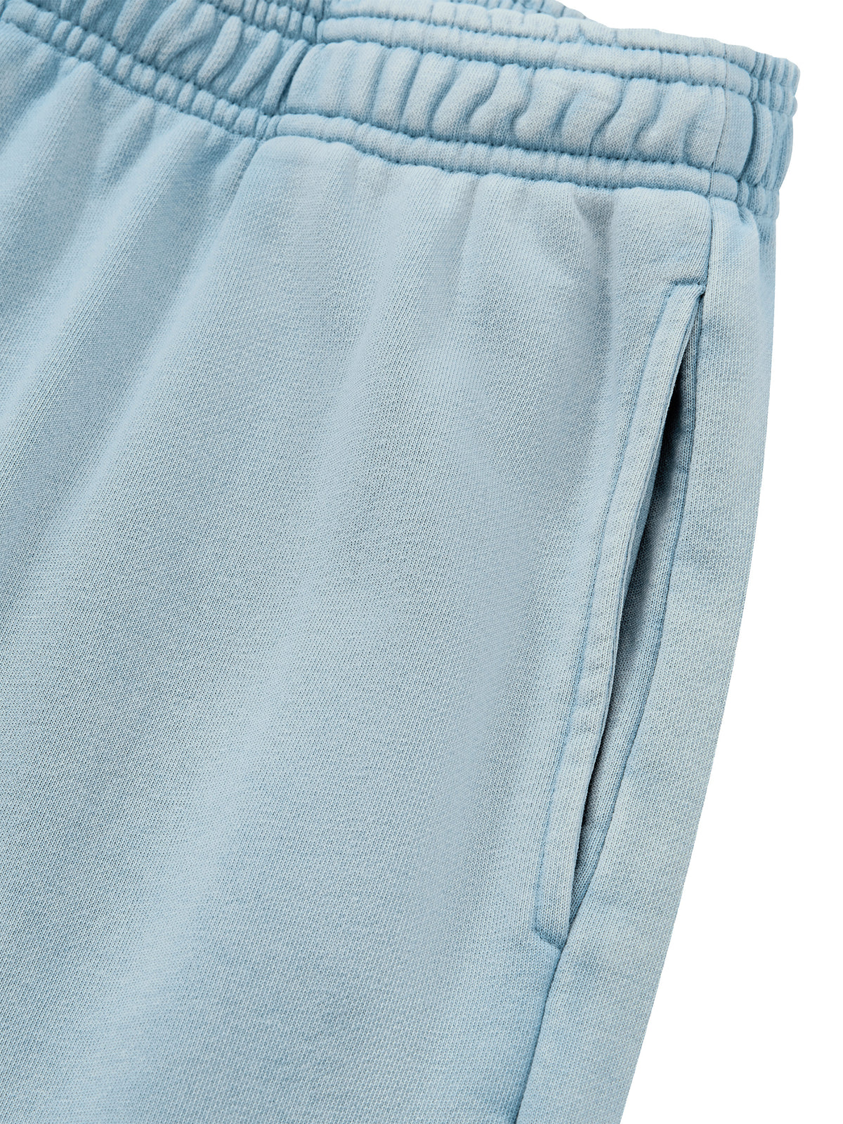 Close-up of light blue sweatpants showing the elastic waistband and side pocket seam on a white background.