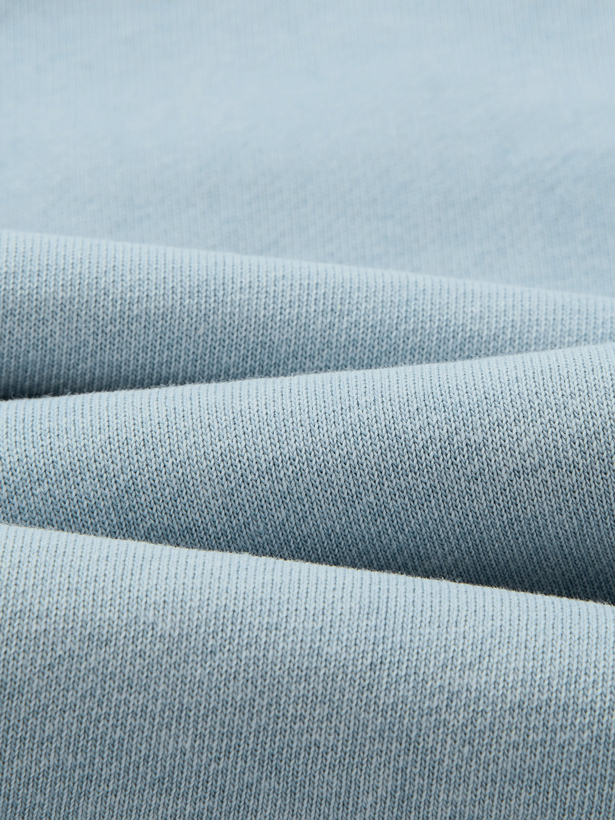 A close-up of light blue knit fabric with soft folds showing the fine woven texture.