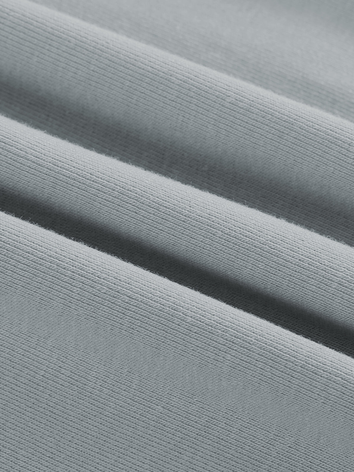 A close-up of light gray ribbed fabric with soft diagonal folds showing the knit texture.